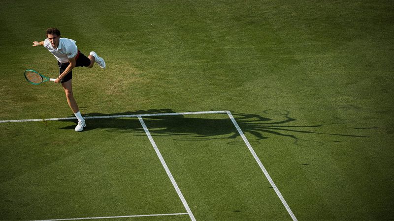 Tennis player reaching for a forehand on grass