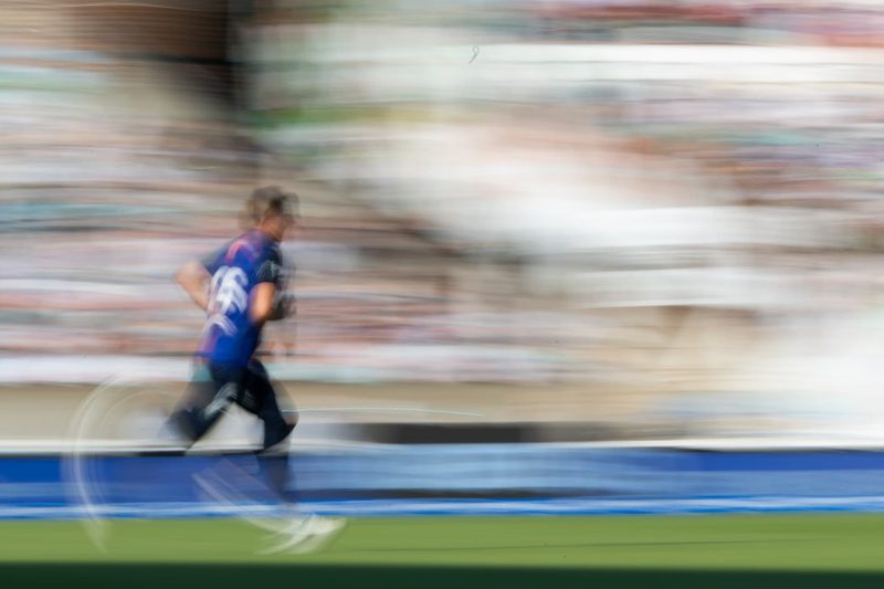 Cricketer running in front of a packed stand, panned motion blur
