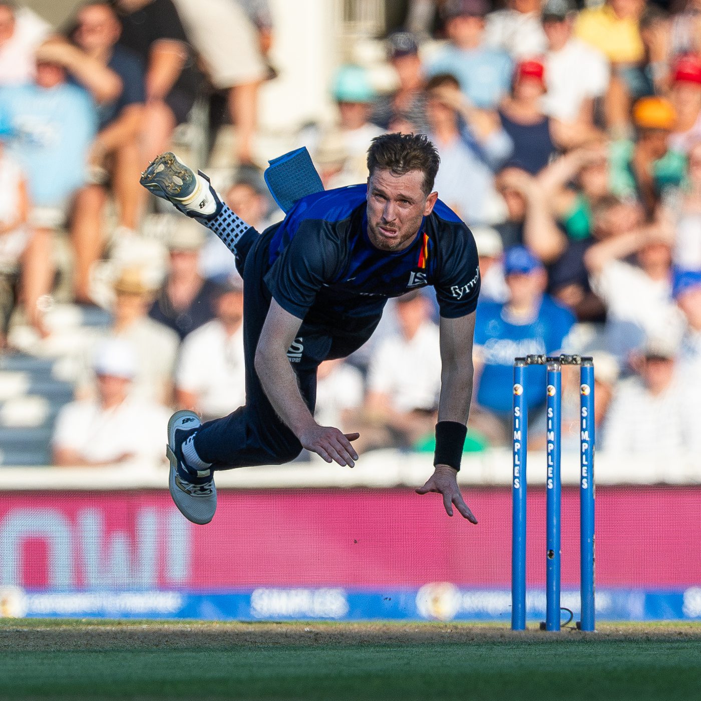 Fast bowler in mid-air follow-through beside the stumps