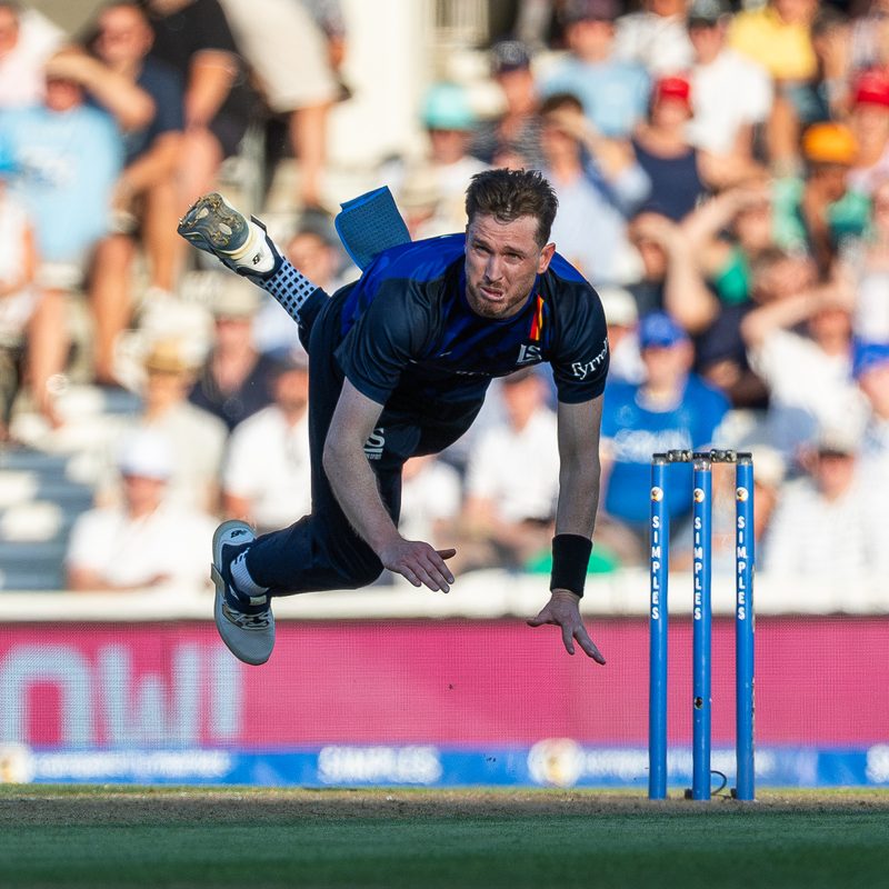 Fast bowler in mid-air follow-through beside the stumps
