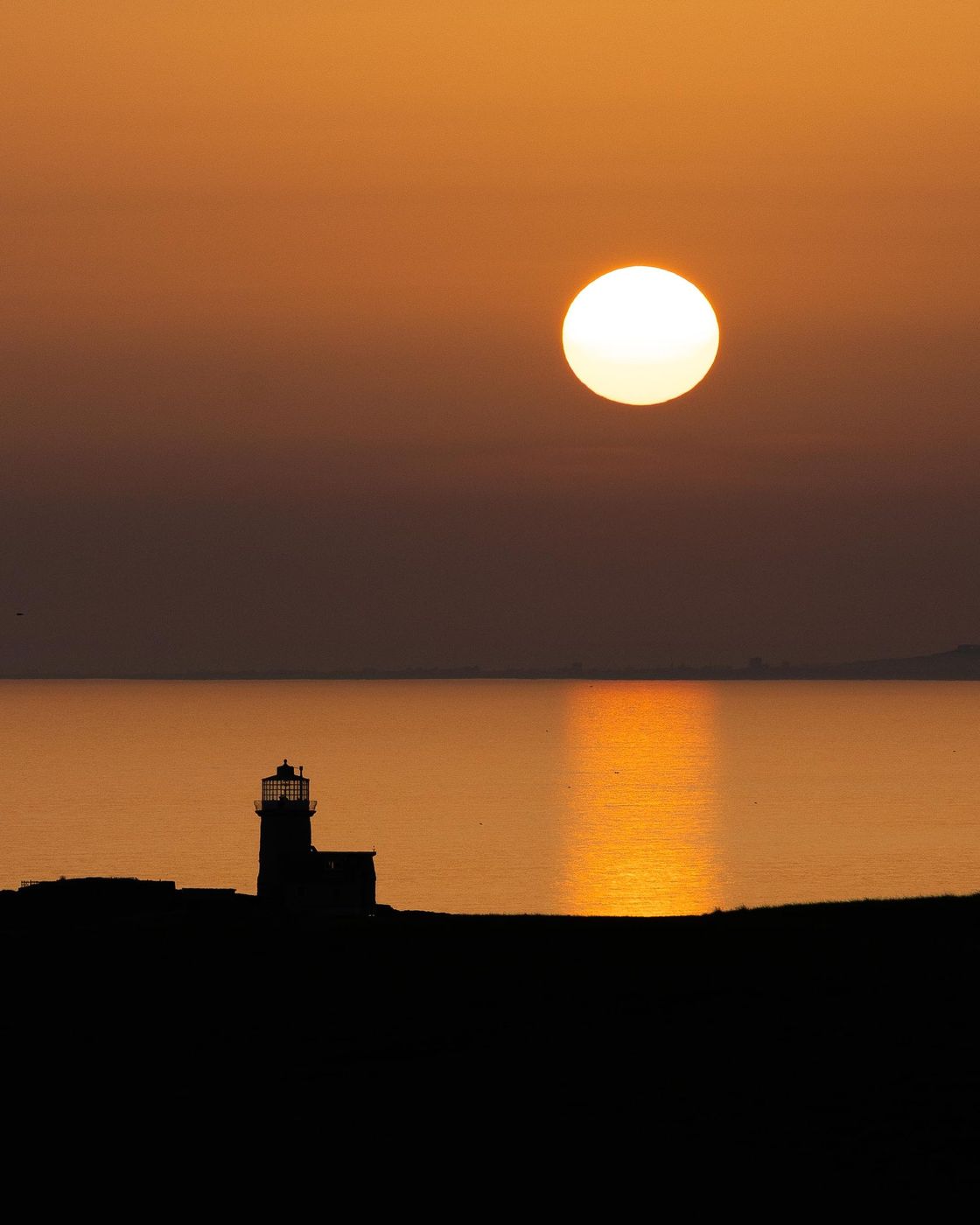 Sun setting over a lighthouse silhouette